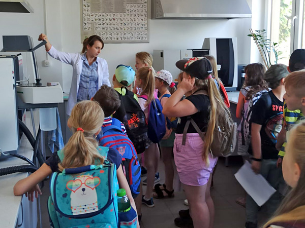 Kobieta w białym fartuchu stoi wśród dzieci w wieku szkolnym w nowocześnie urządzonym laboratorium
