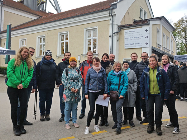 Grupa uśmiechniętych osób pozuje na tle zabytkowego budynku kopalni